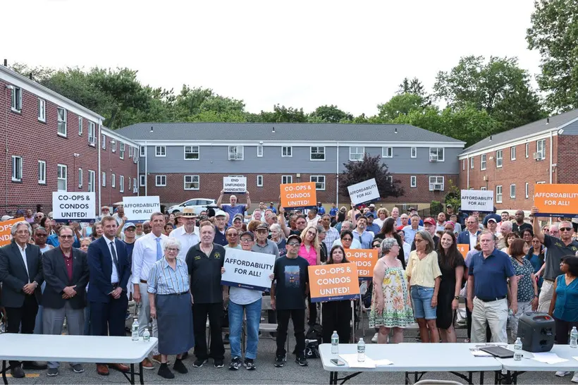 A large group of people stand outside in front of Bell Park Manor Terrace holding signs stating "Co-ops & Condos United!" and "Affordability for All!"