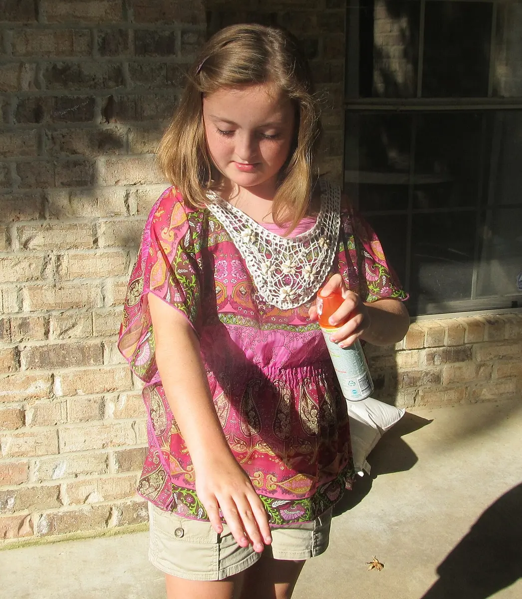 A girl applies insect repellant to her arm.