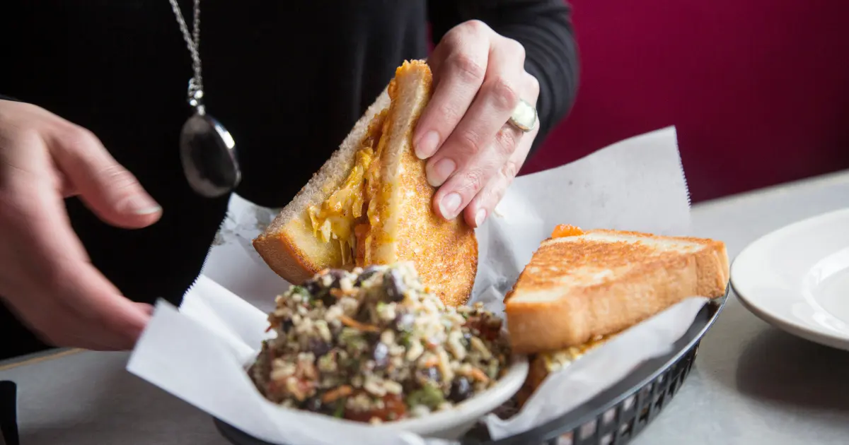 A person's hand lifting a sandwich next to a small bowl of caramelized onions Credit: Derek Davis/Portland Portland Press Herald via Getty Images via Sentient.