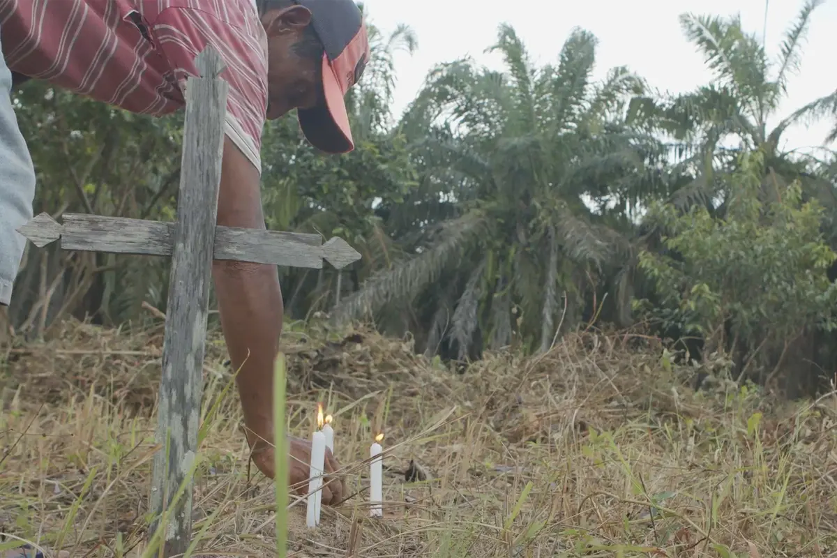 Indigenous laborer Francisco Neves Costa lights candles at a grave with oil palm trees in the background at the Livramento Cemetery. Image by Mongabay.