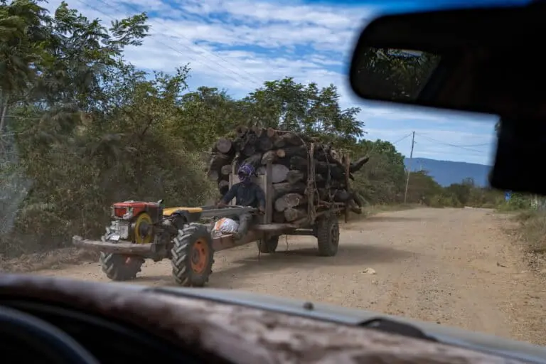 Reporters watch from a car as logs are transported by koy-yun on the road that connects the Cardamom Mountains to Chbar Mon. The wood will likely be sold to a network of middlemen at Chbar Mon, who then sell it onto factories in Kampong Speu and Phnom Penh that incinerate the wood to generate steam. Image by Andy Ball for Mongabay.