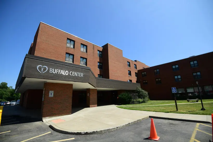 A photo of Buffalo Center for Rehabilitation and Nursing from the outside, showing the front of the building and a parking lot with an orange traffic cone.