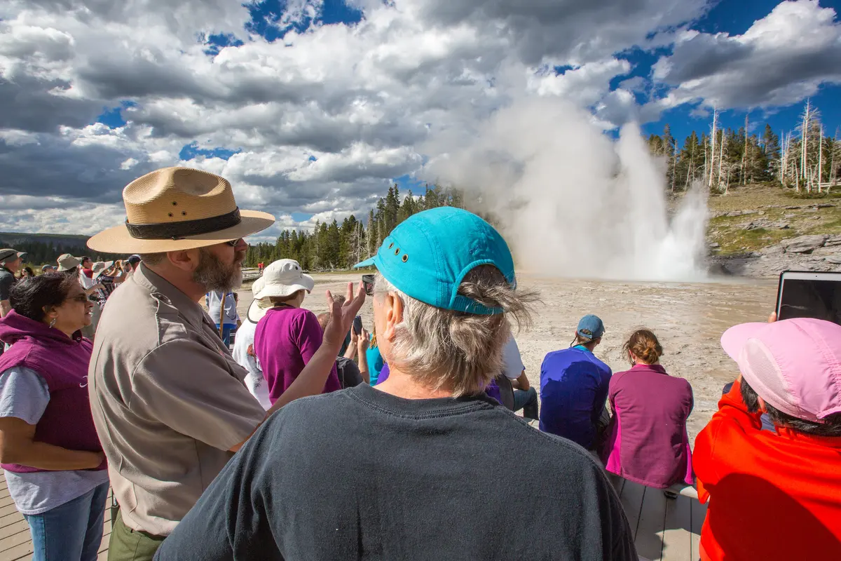 Ranger explains the mechanics of geysers, while a "grand" example erupts in the background NPS photo by Neal Herbert