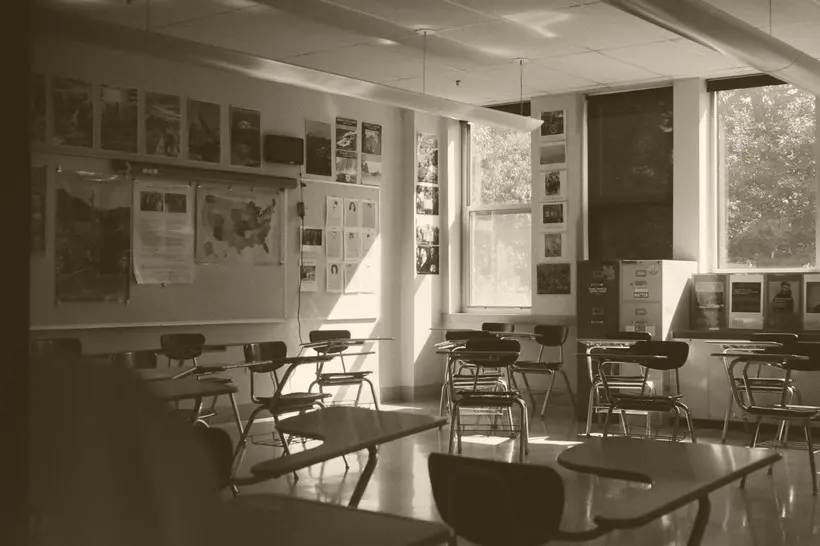 An image of a classroom with two windows and many empty desks.