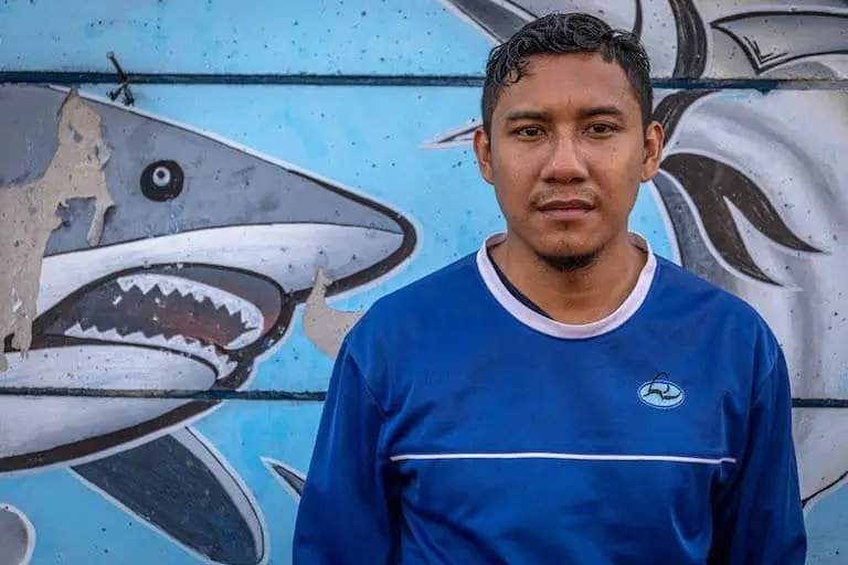 Former deckhand Adhi Tayuh Braka stands in front of a mural at Tanjung Emas Harbor in Semarang, Indonesia, in September. His shirt bears DOF’s logo. Image by Aji Styawan for Mongabay.